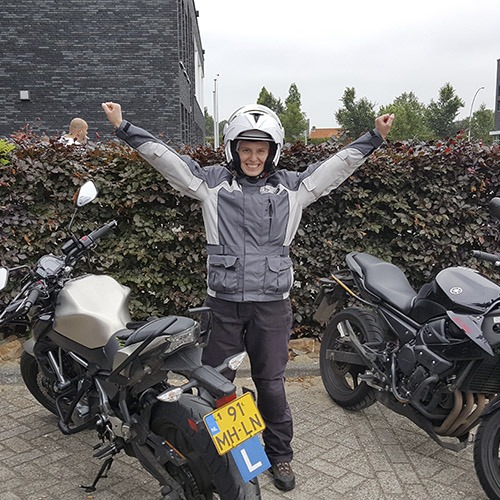Geslaagde leerling met de armen in de lucht naast de motor