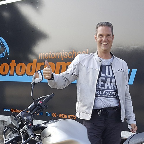 Geslaagde leerling steekt zijn duim op bij de bus van Motodrome